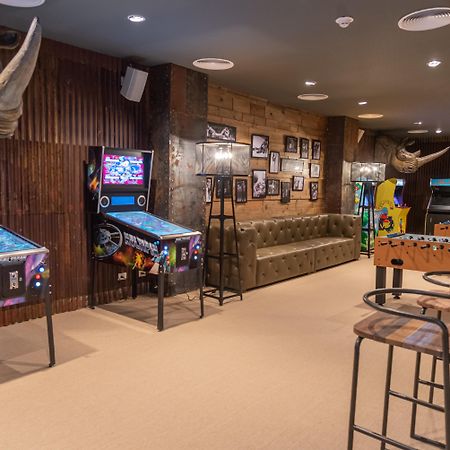 Grand Bavaro Princess (Adults Only) Exterior photo The photo shows a game room with a cozy and fun atmosphere. On the left side, there are two pinball machines with colorful graphics. A tufted green sofa is situated against the wall, providing a comfortable seating area. The walls are decorated with 