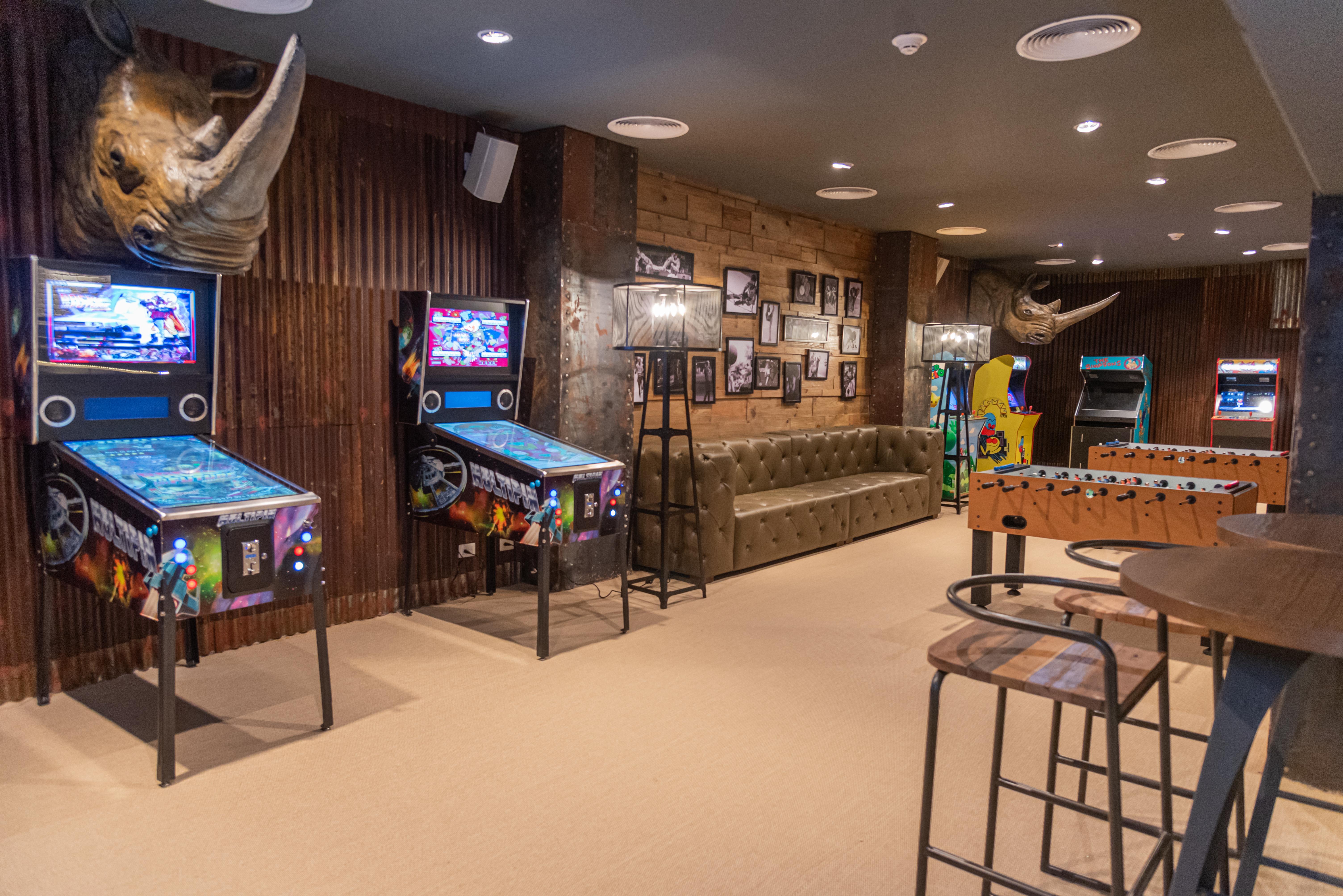 Grand Bavaro Princess (Adults Only) Exterior photo The photo shows a game room with a cozy and fun atmosphere. On the left side, there are two pinball machines with colorful graphics. A tufted green sofa is situated against the wall, providing a comfortable seating area. The walls are decorated with 